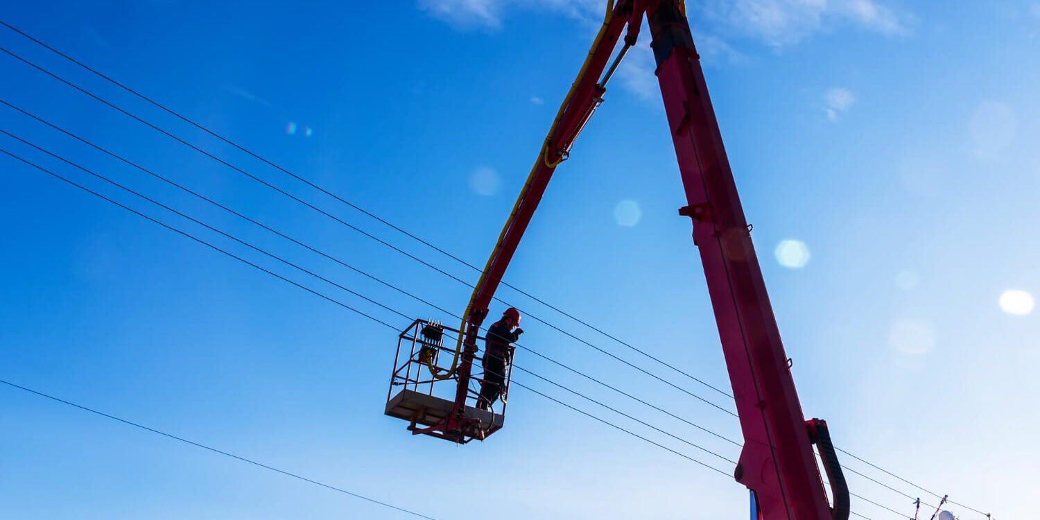 electrician-worker-working-at-height-on-hydraulic-aerial-platform-against-blue-sky