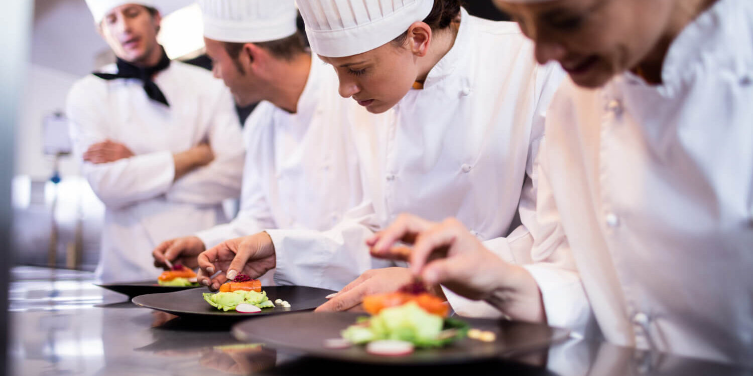 head-chef-overlooking-other-chef-preparing-dish